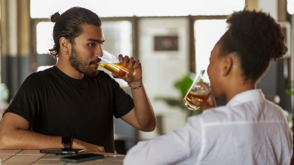 A man and woman sitting at a bar drinking beer.