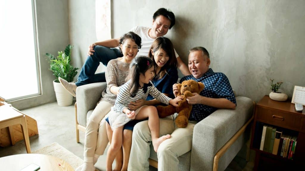 A family happy together as they sit on a couch while the older man holds a teddy bear.