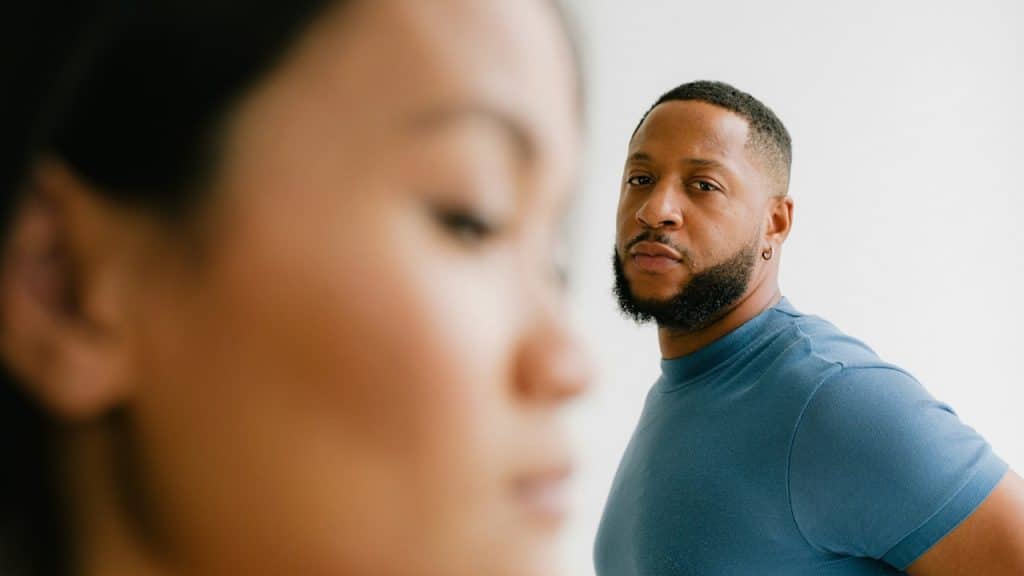 A bearded man staring at a woman standing in the foreground.