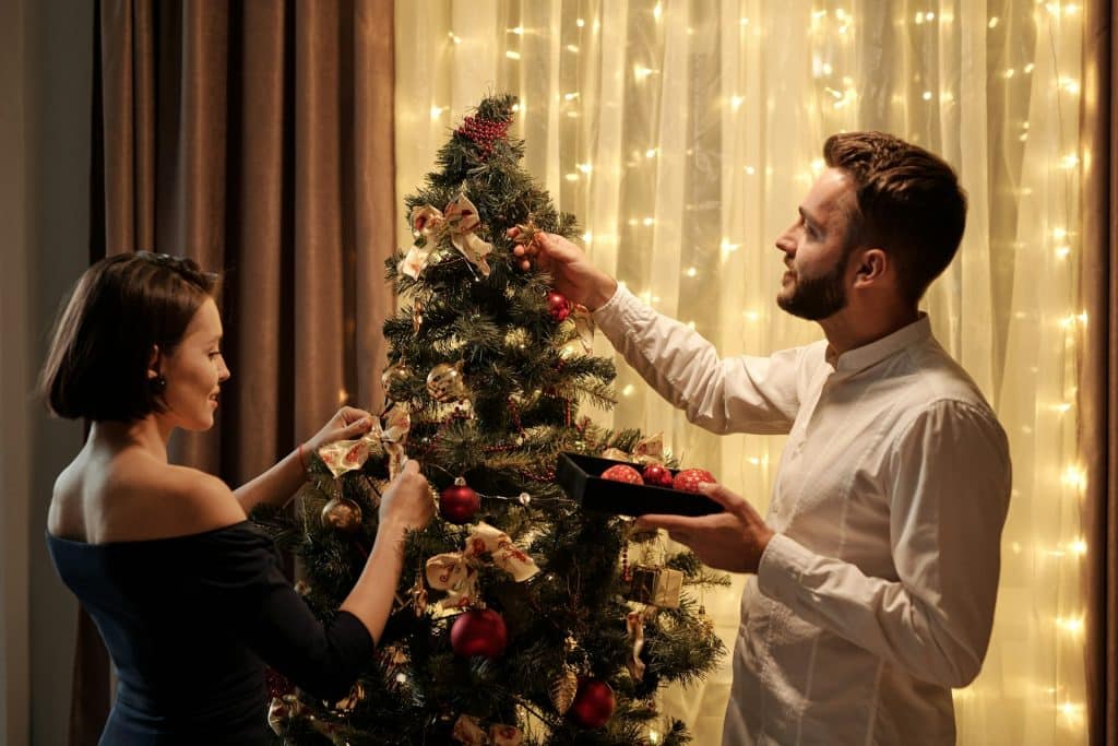A man helping the woman decorate the Christmas tree.