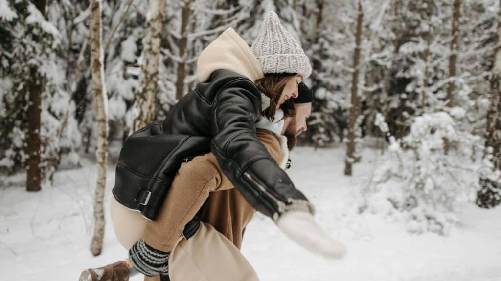A man carrying the woman on his back in a snow-covered forest.