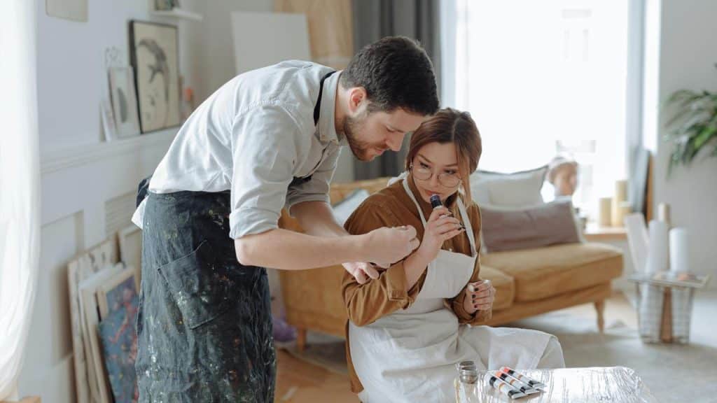 A man and woman in aprons look at a paint bottle together in an art studio.
