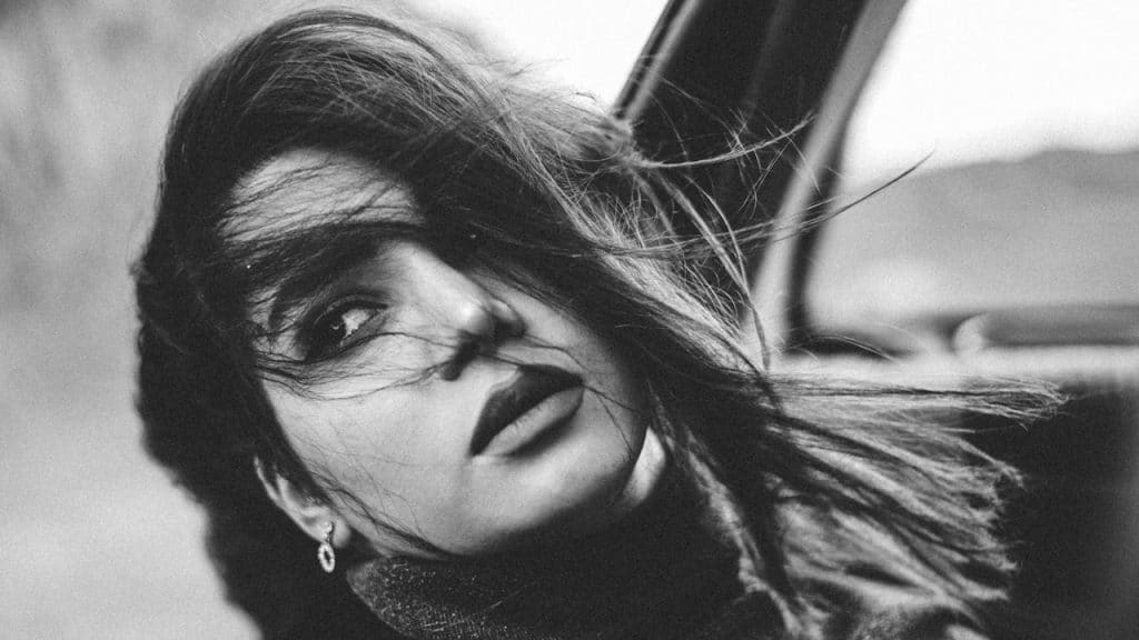 A black-and-white photo of a woman sticking her head out of a car window.