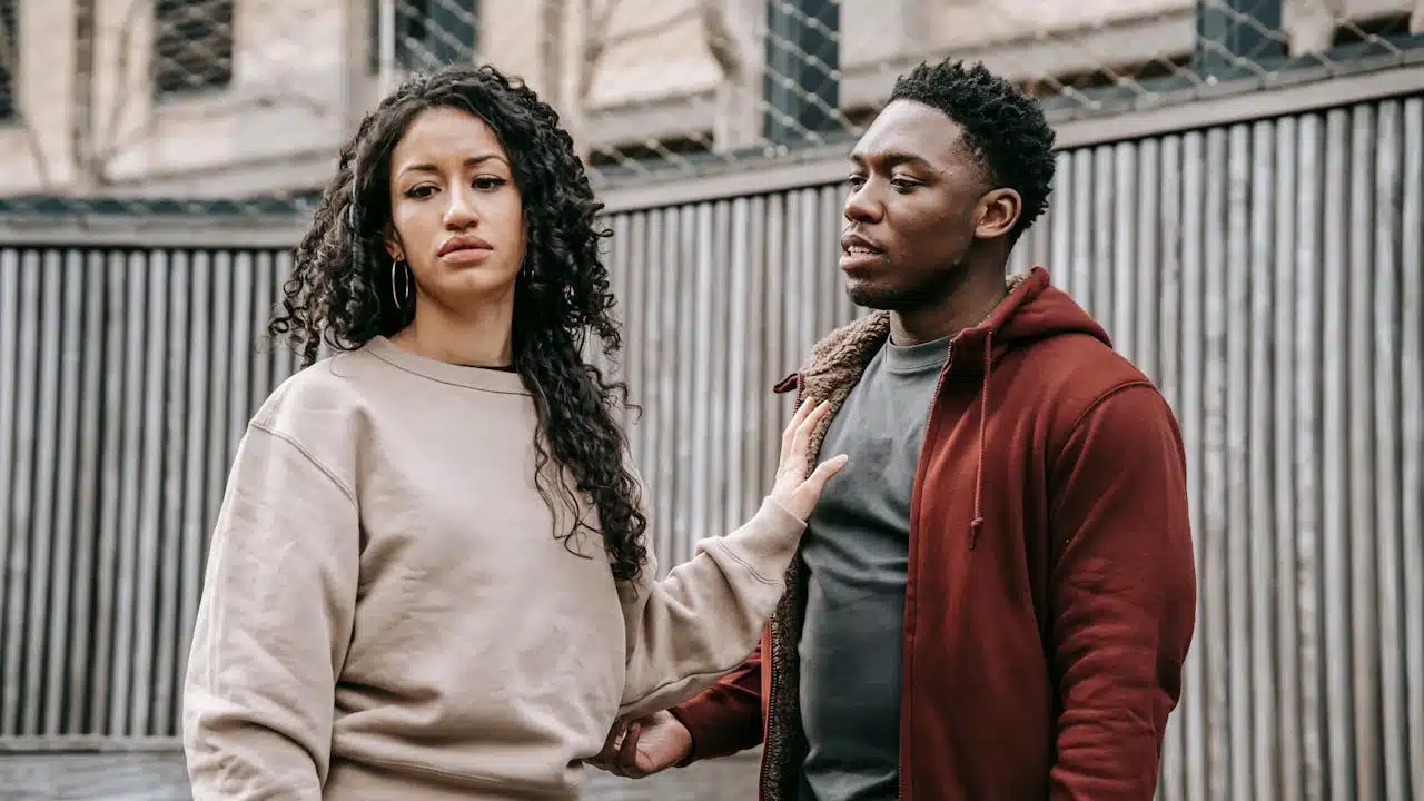 A woman looking away with an expression of displeasure while a man touches her arm gently.