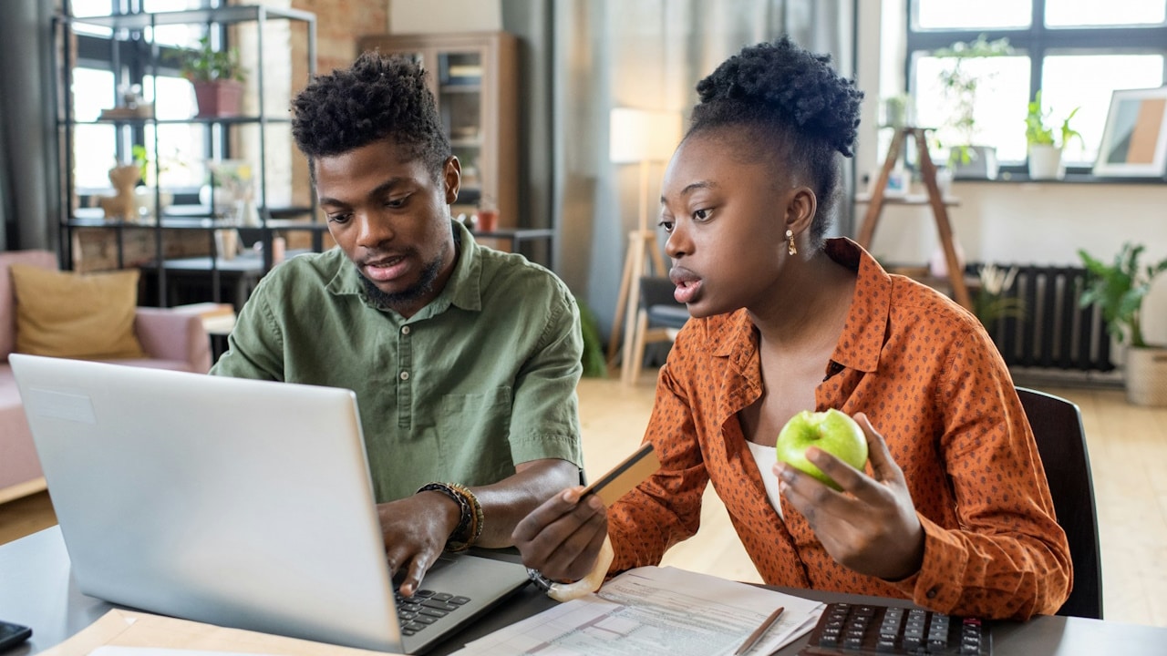 A couple sitting at a table with papers and using a laptop while filling out a tax refund form online.