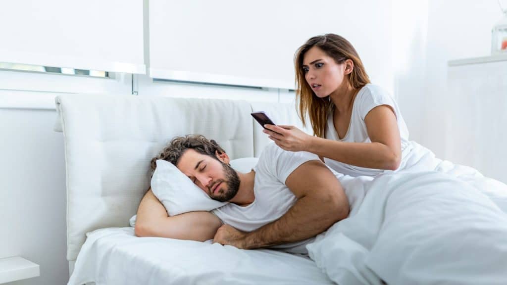A woman reading text messages of her husband while he is sleeping.