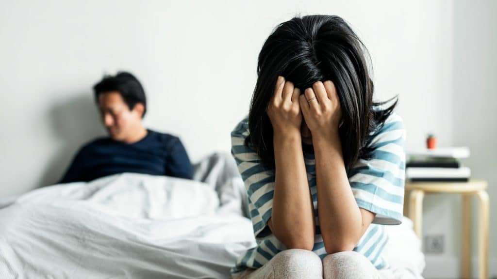 A woman is sitting on the edge of a bed while her husband is sitting at the end of the bed.