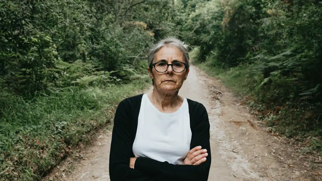 A woman standing on a dirt road in the trees.