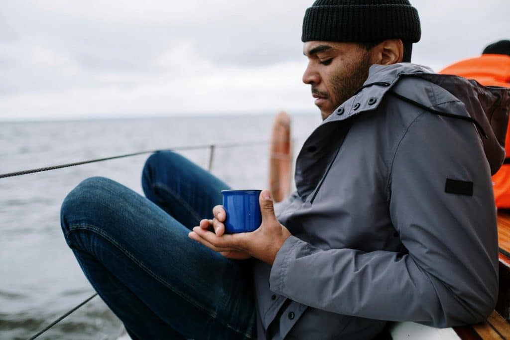 A man holding a blue ceramic mug while sitting on the boat.