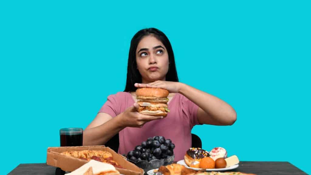 A woman holding a burger with a table full of junk food in front of her.