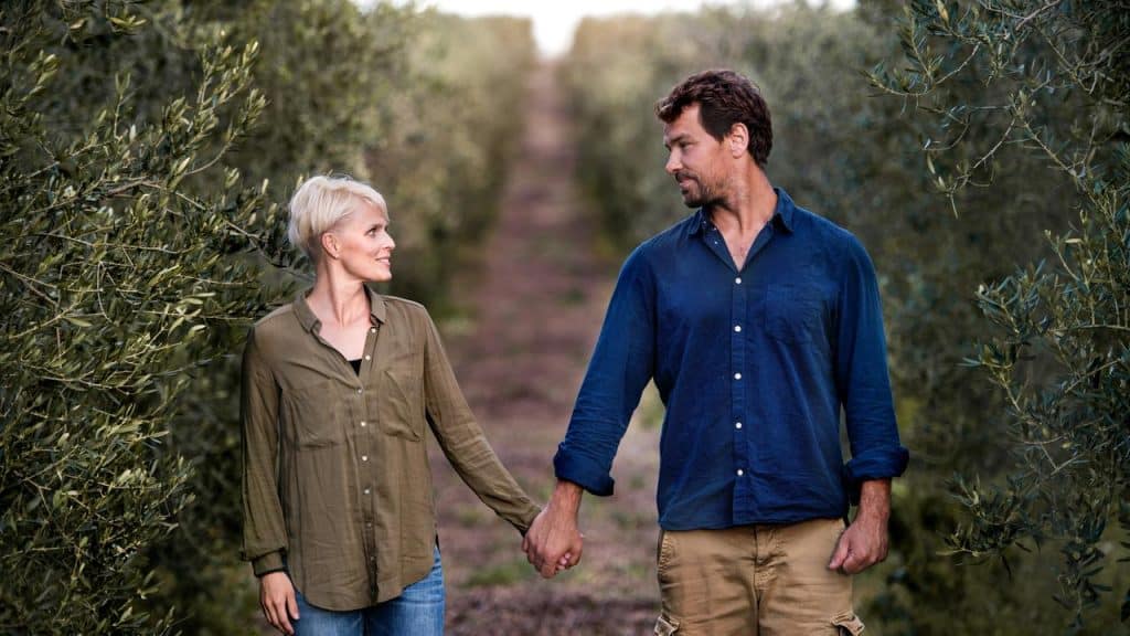 A couple holding hands as they stand in the middle of a garden.