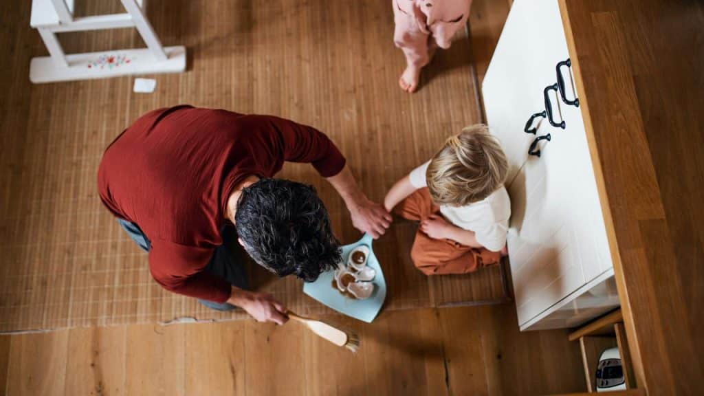A man cleaning up spilled drinks on the floor while a child sits nearby.