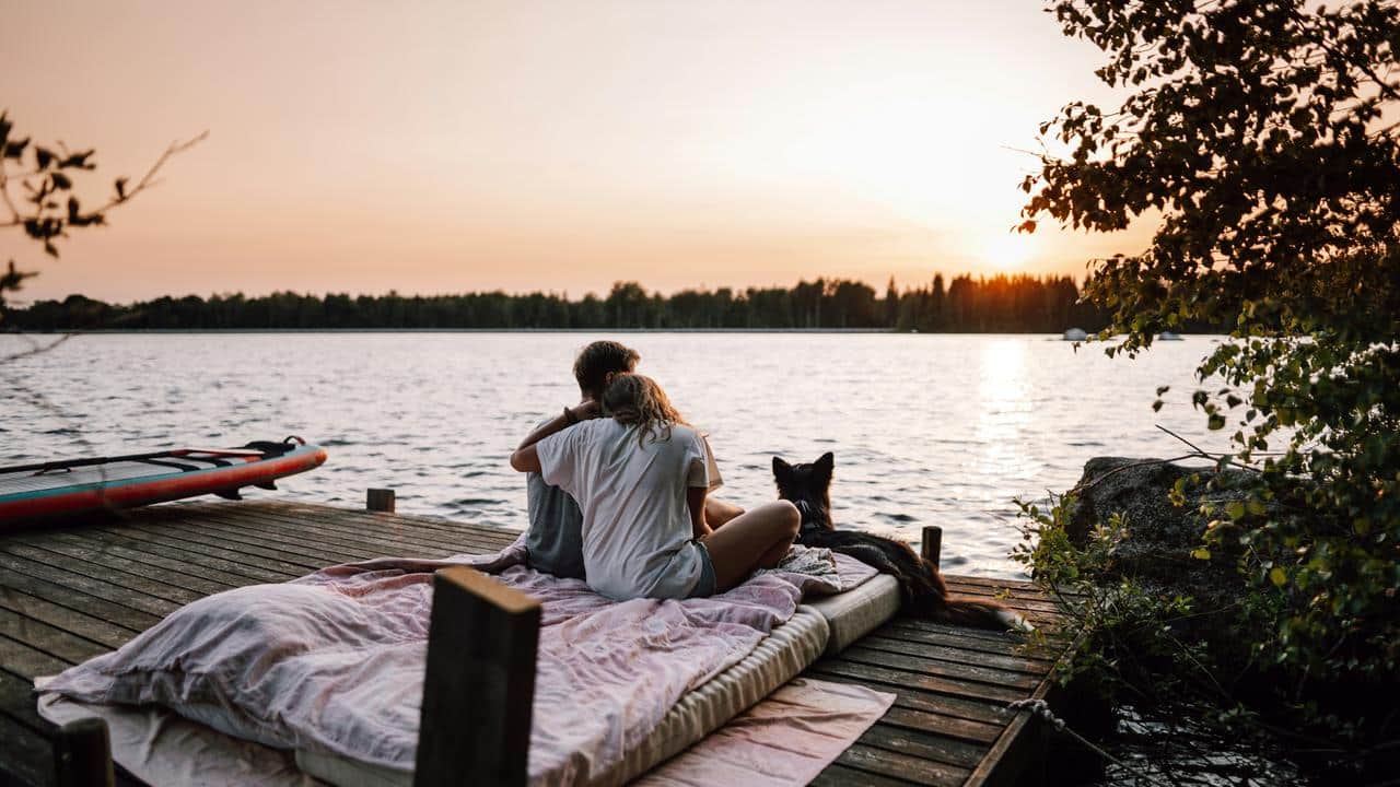A couple sitting with their dog on a dock watching the sunset over a lake.