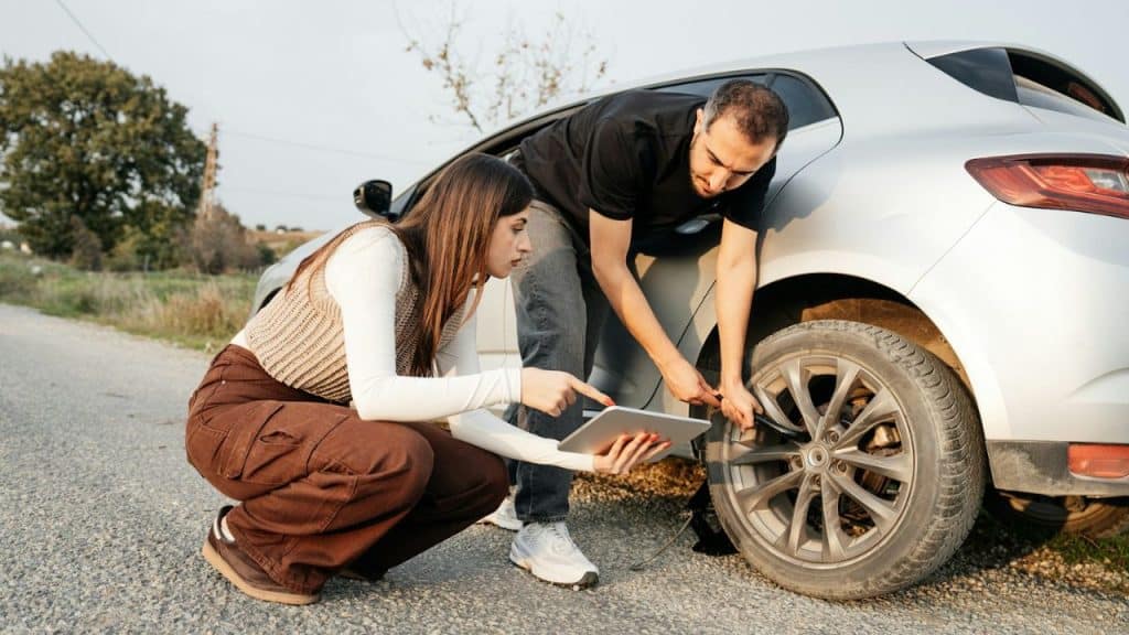 Man inflating a silver car tire while a woman points at a tablet beside him.
