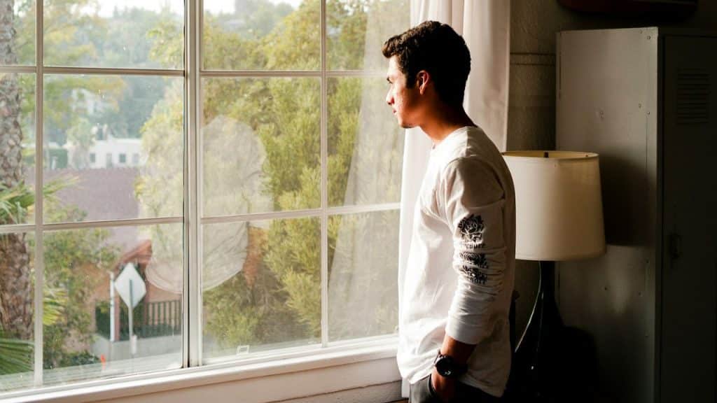 A man in a white long-sleeve shirt looks out a window.