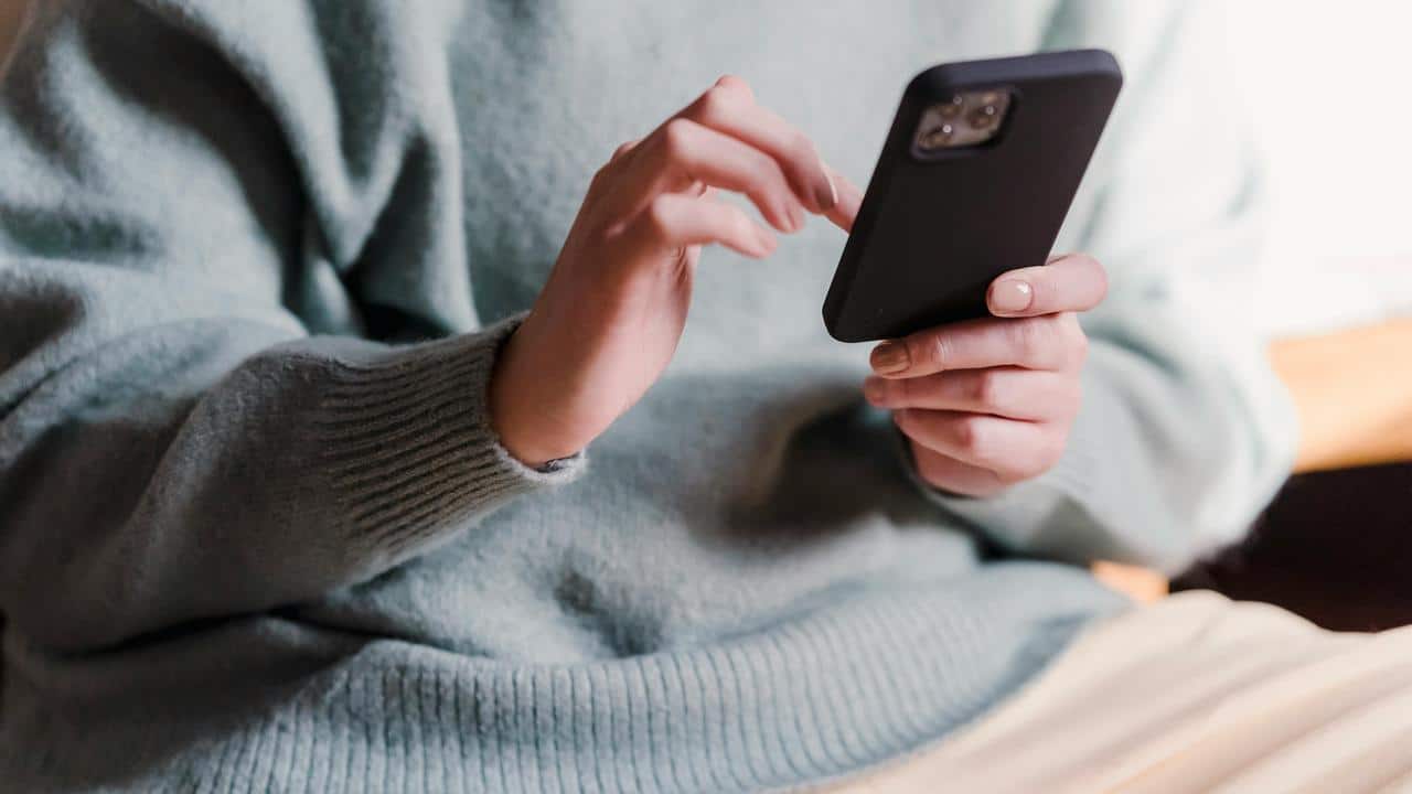 A person wearing a light sweater using a smartphone.