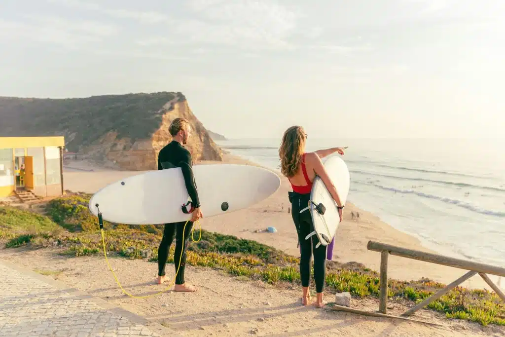 A man and a woman holding surfboards at the beach.