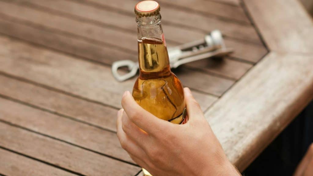 A hand holding a glass bottle on a wooden table.