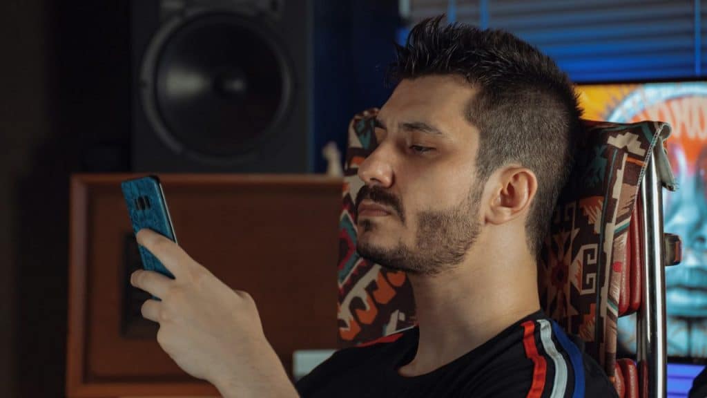 Man with dark hair and a full beard sits in a dark room looking away.