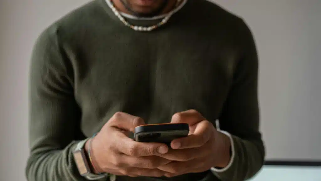 A man in a dark green sweater using a smartphone.