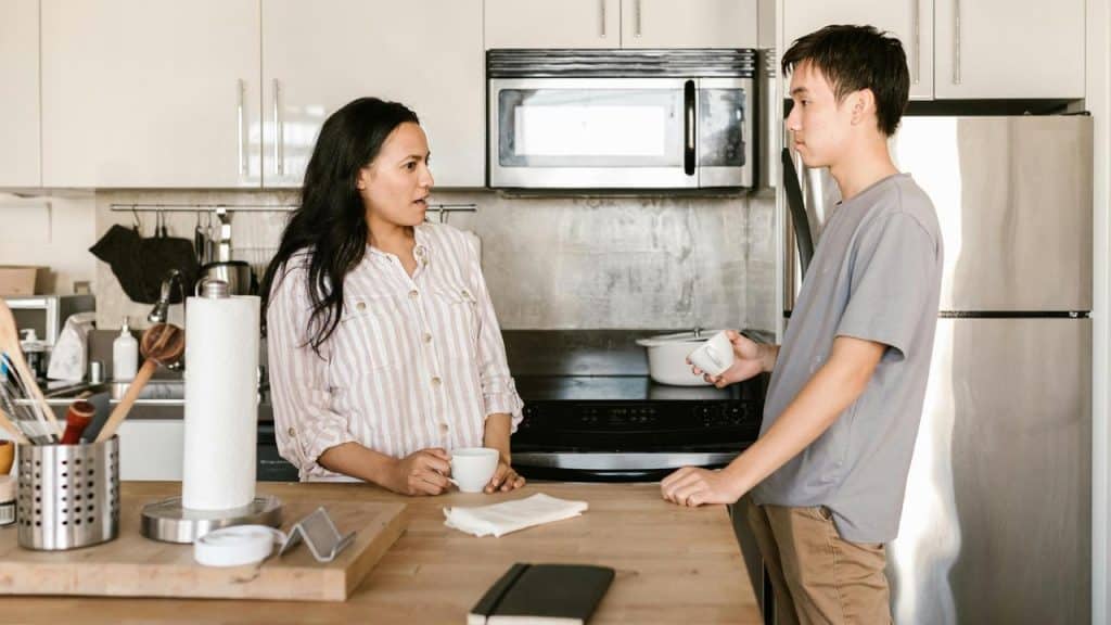 A woman and a man talking in a kitchen while holding cups.