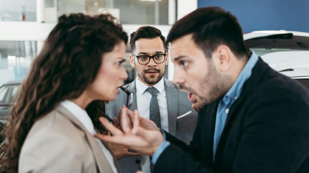 A man shouts at a woman while another man in glasses looks shocked between them.