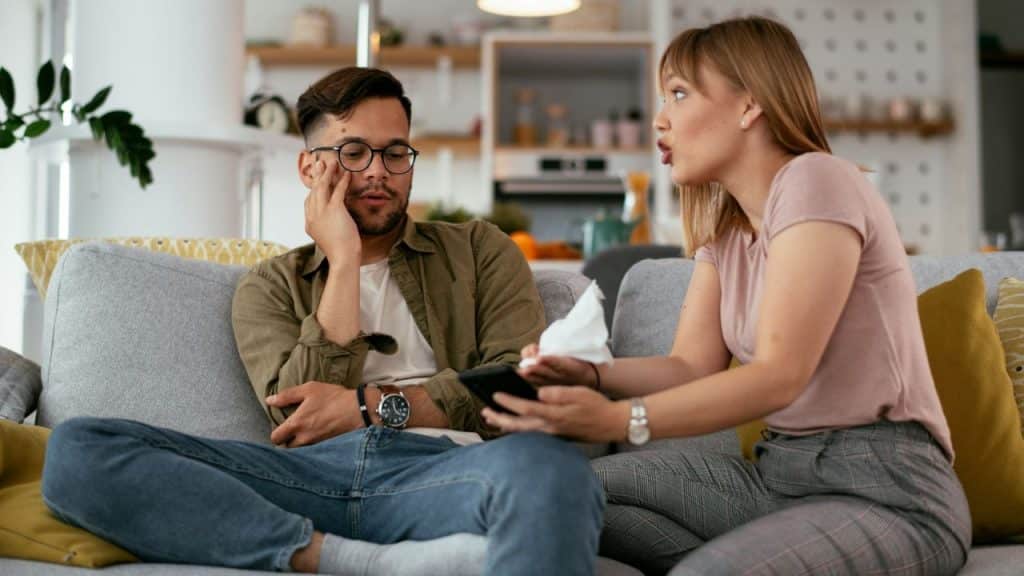 A woman gestures while speaking to a man who looks away with a hand on his face.