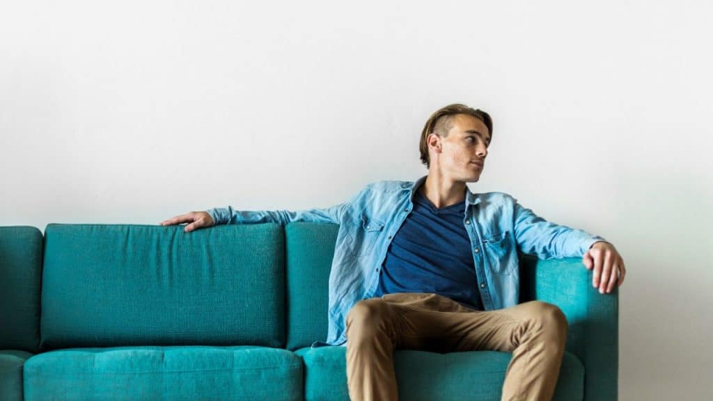 Man in a light blue shirt and brown pants relaxing on a turquoise couch.