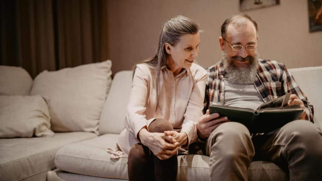 A senior couple sitting on a couch, looking at a photo album together.