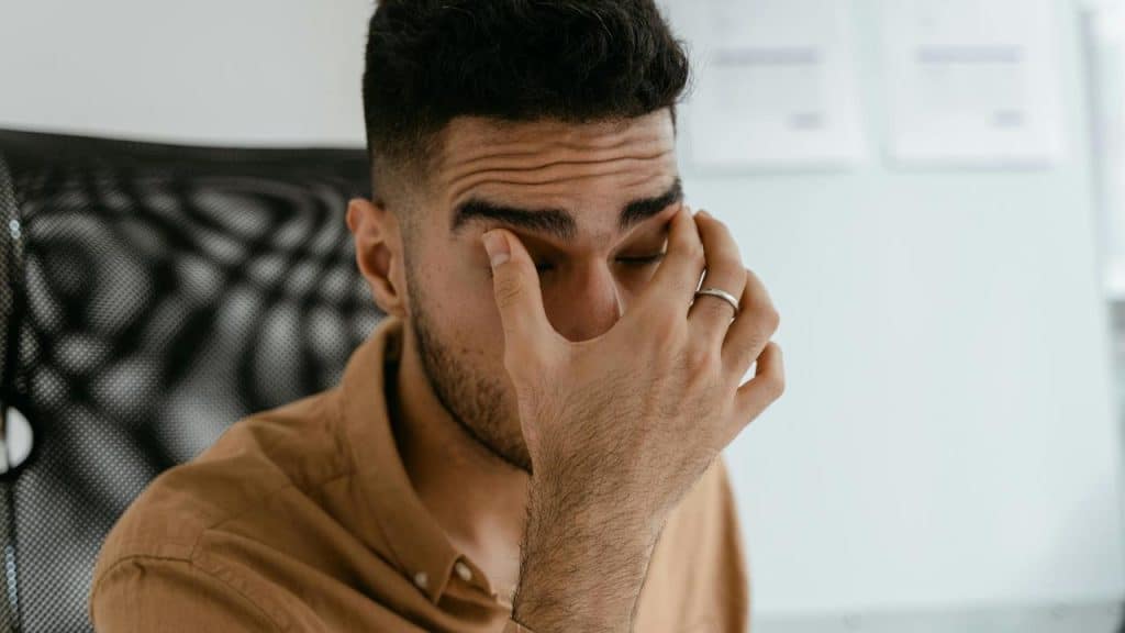 A man sitting at a desk with his hand covering his eyes.You can’t heal something you refuse to look at. Some memories sit in the corner like they vanished, but they didn’t. They’re still hanging around, waiting for a moment to show up in your choices, your reactions, your conversations.