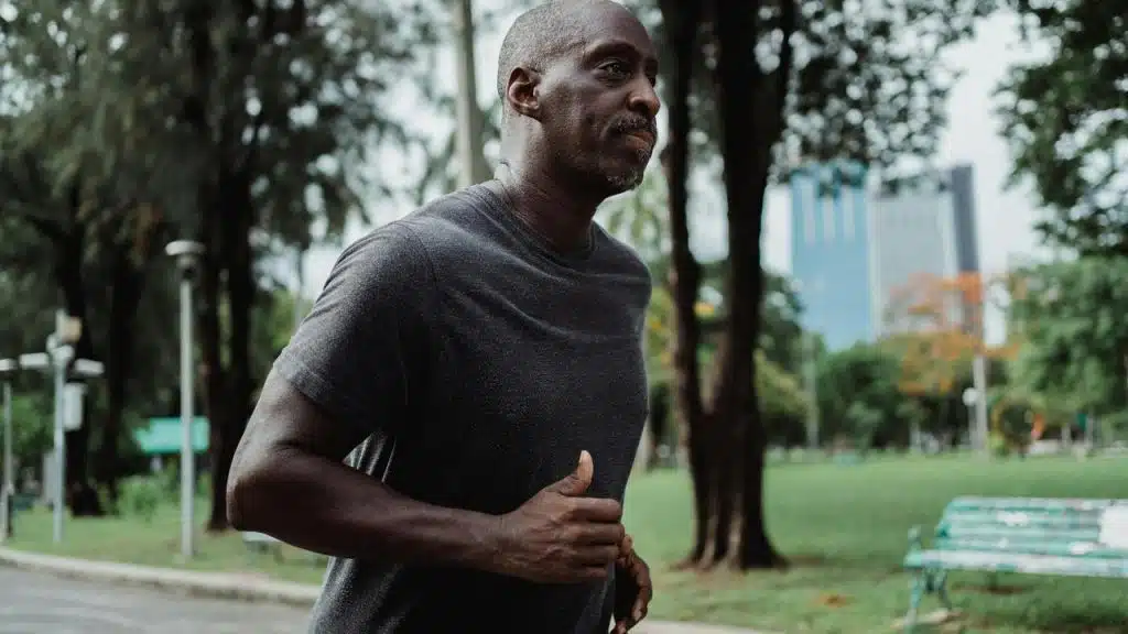 A man jogging through a park with trees and buildings in the background.