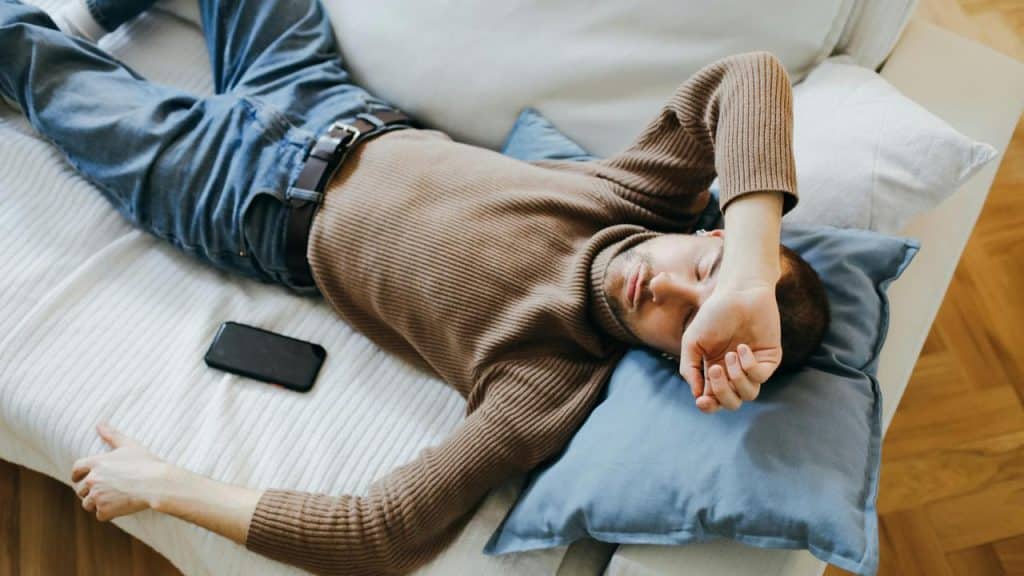 A man lying on a couch with his arm over his eyes.