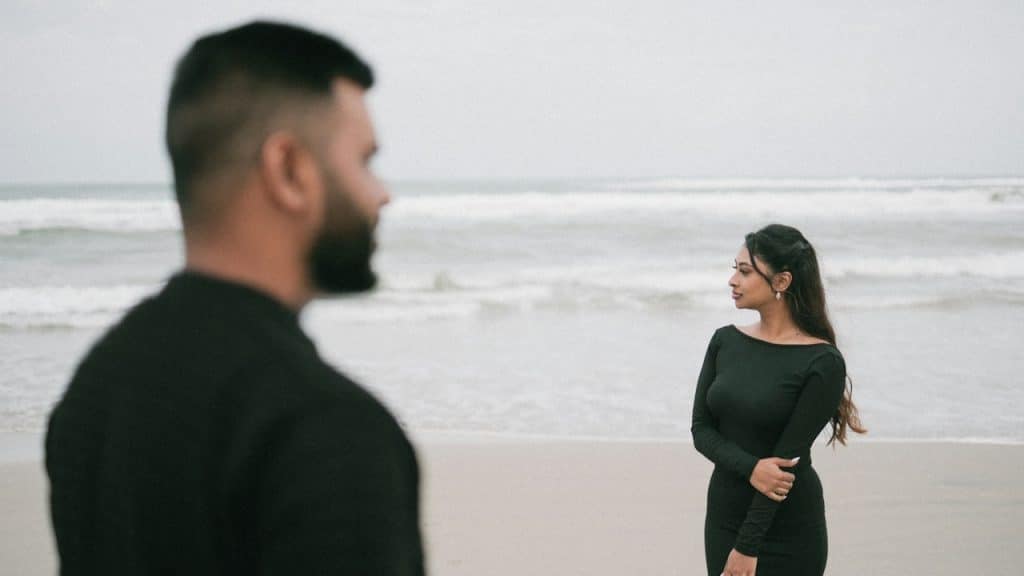 A man and a woman in black dresses standing on a beach.