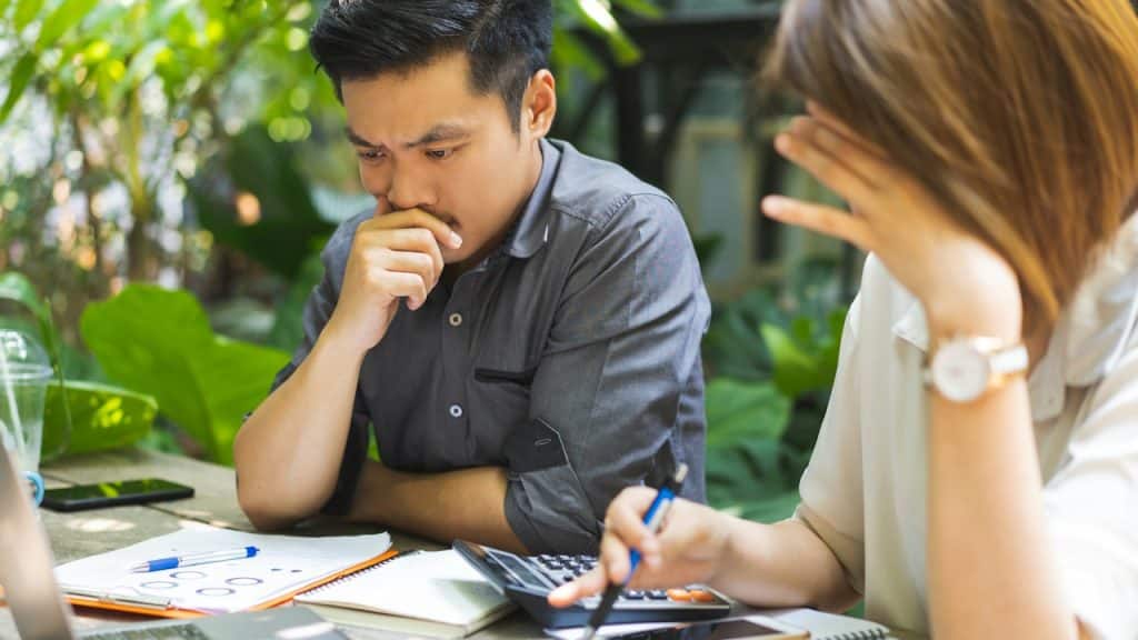 A stressed man is sitting at a table with documents and a calculator.