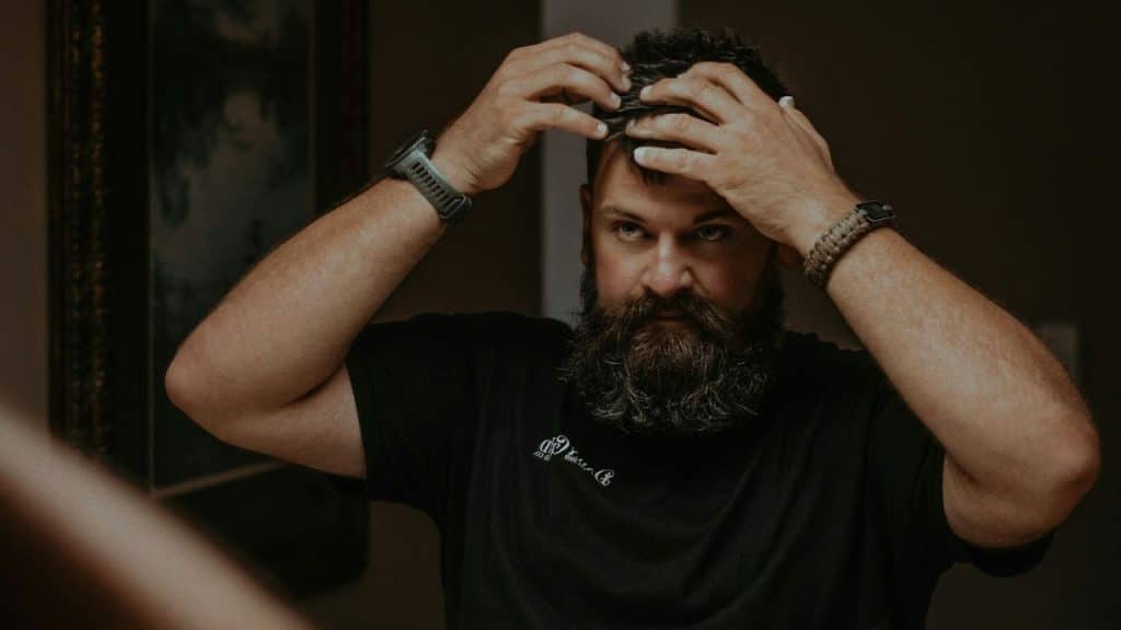Man with a long beard fixing his hair while looking into a mirror.