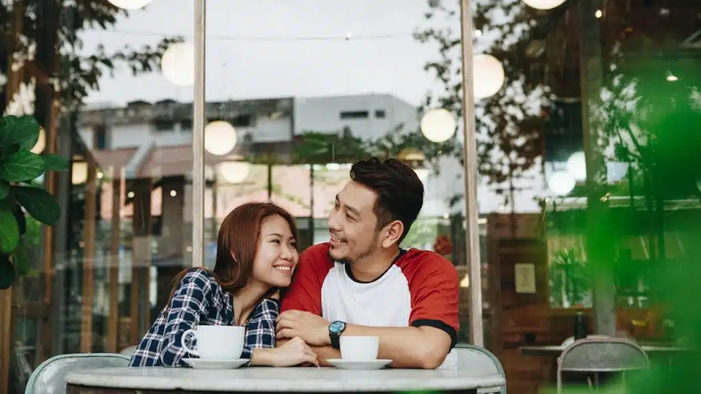 A woman holding a man’s arm while they sit at a table outdoors and have coffee.