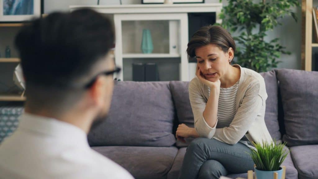 Woman with short hair sitting on a sofa, leaning on her hand, talking to a man.
