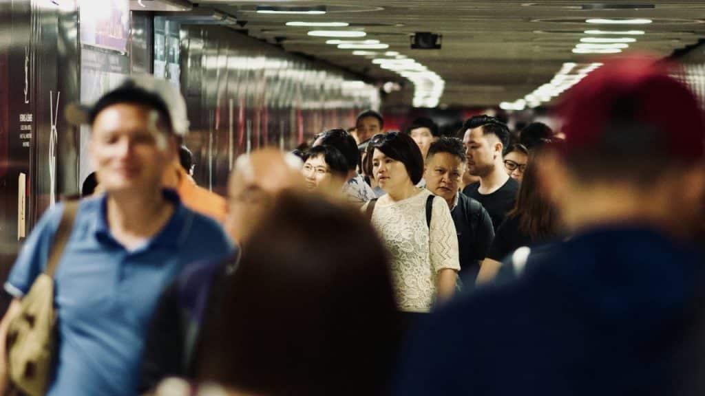 A blurry crowd of people walking down a narrow, brightly lit indoor hallway.