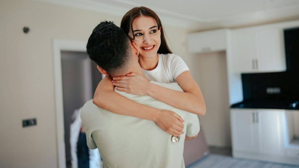 Happy young woman hugging a man and holding keys in a bright, modern room.