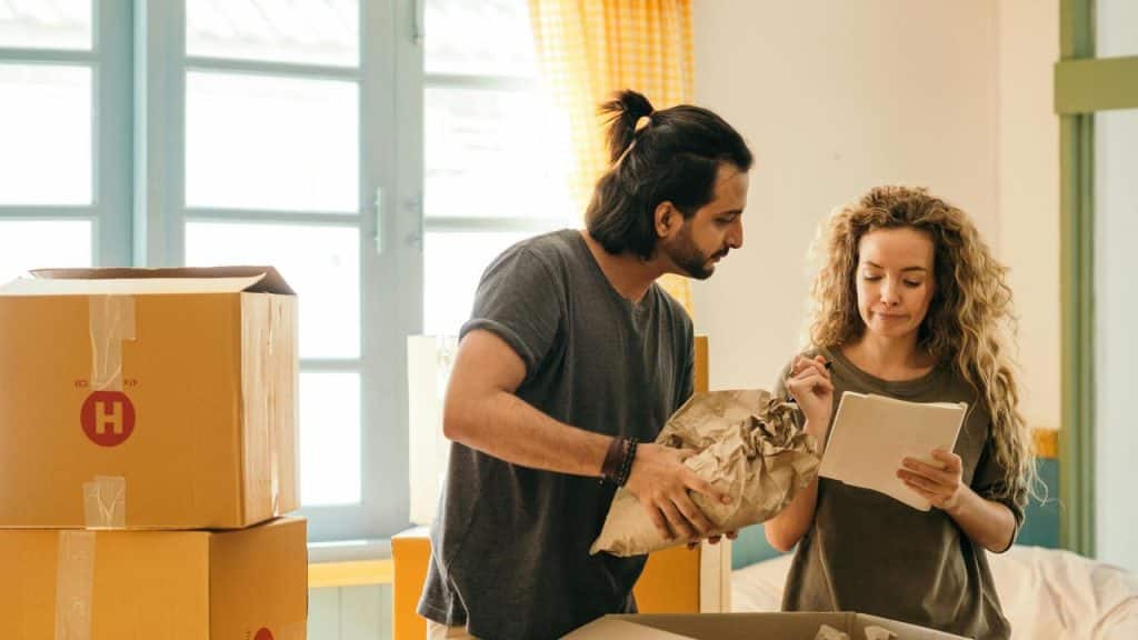 A couple unpacking boxes together in a sunlit room.