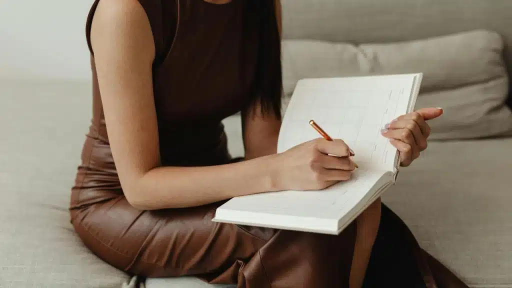 A woman writing in a planner while sitting on a couch.