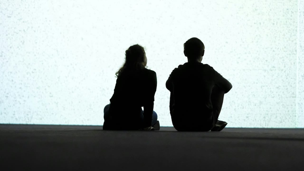 A couple sitting together cross-legged on the ground and staring at a wall. 