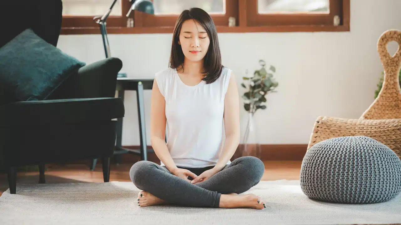 An attractive Asian woman practicing meditation at home in the living room.