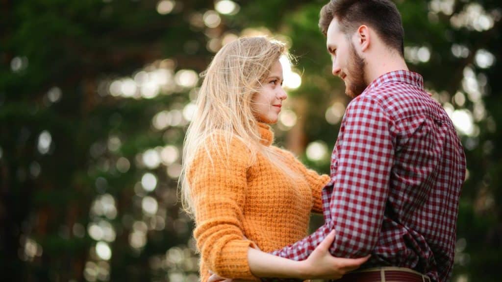 Young couple in casual clothes embracing and gazing at each other outdoors.