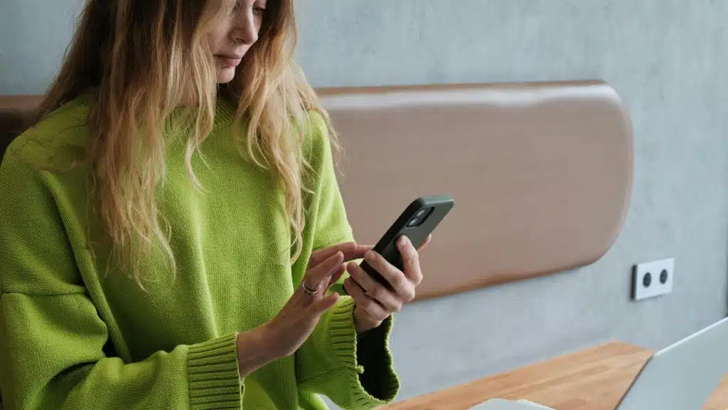 A woman in a green sweater using a smartphone at a table.
