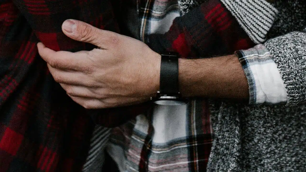 A close-up of a person hugging someone in plaid and knit clothing.