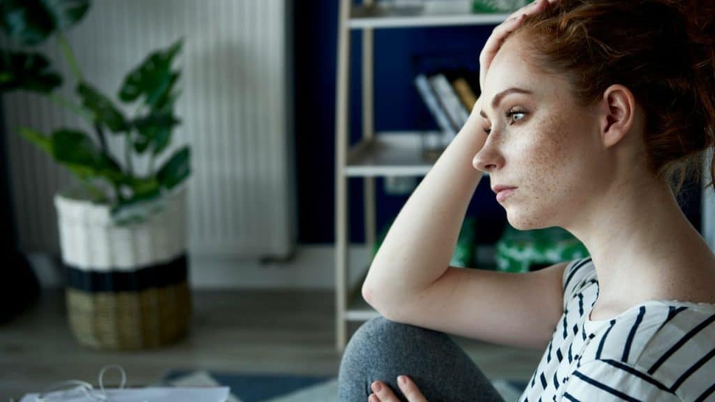 Profile of a young woman with freckles resting her head on her hand indoors.