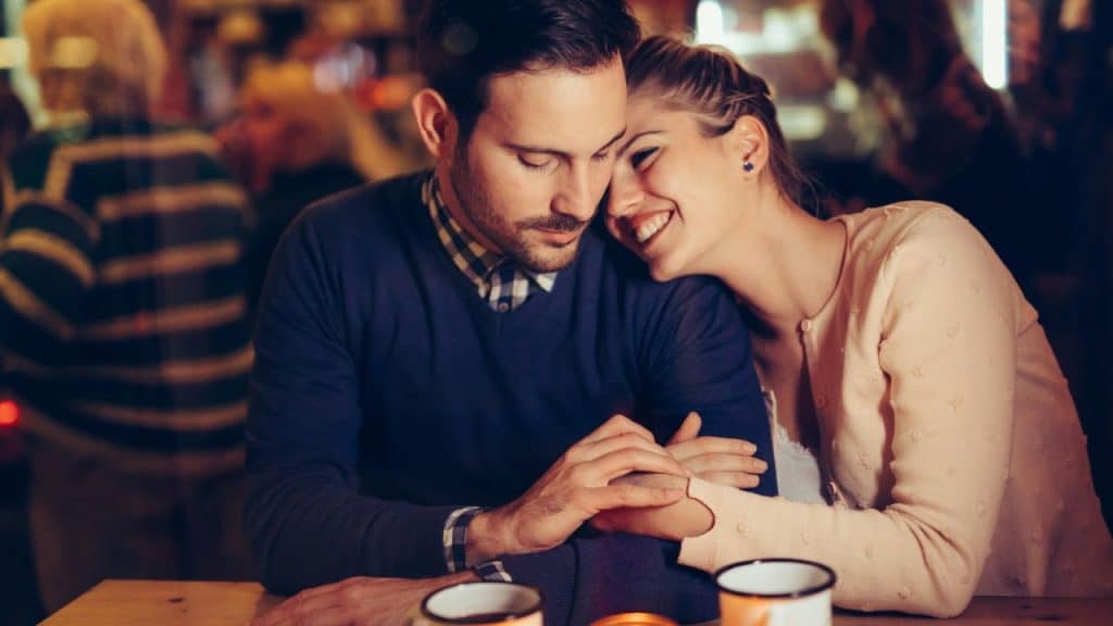 Couple sitting close in a dimly lit bar, woman smiling and leaning on the man.