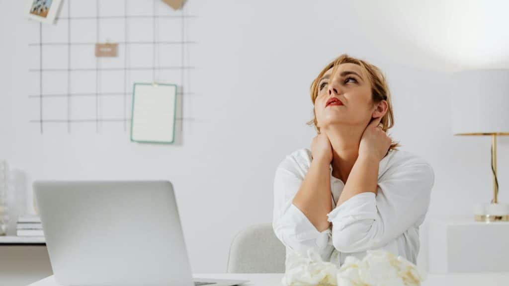 A woman at a desk holding her neck and looking stressed.