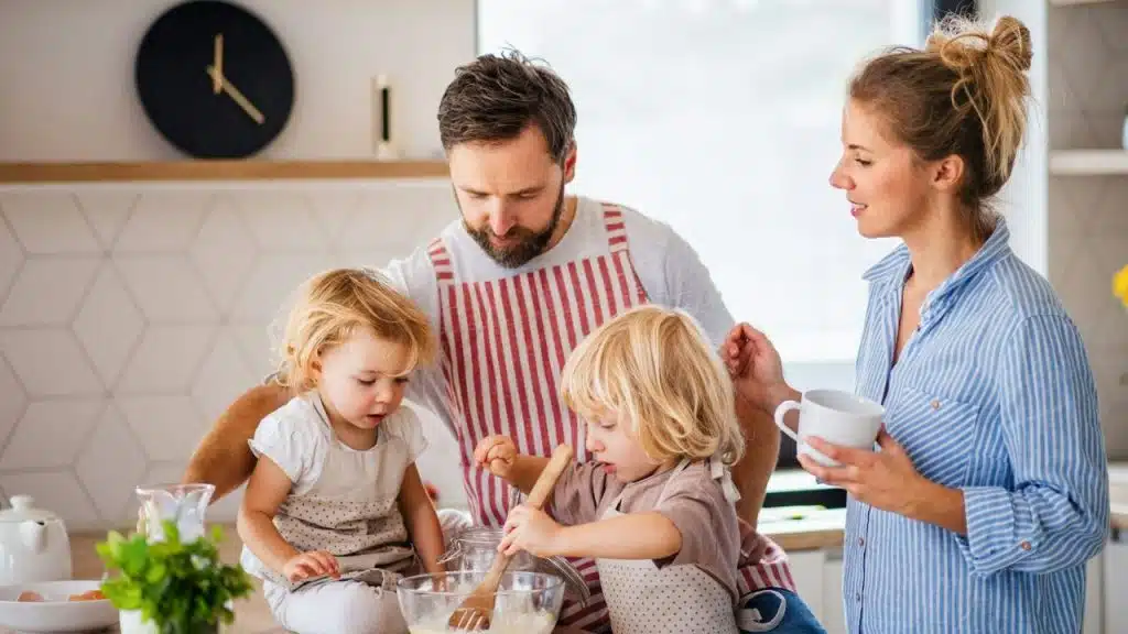 A family of four, including two young children, bakes together in a kitchen.